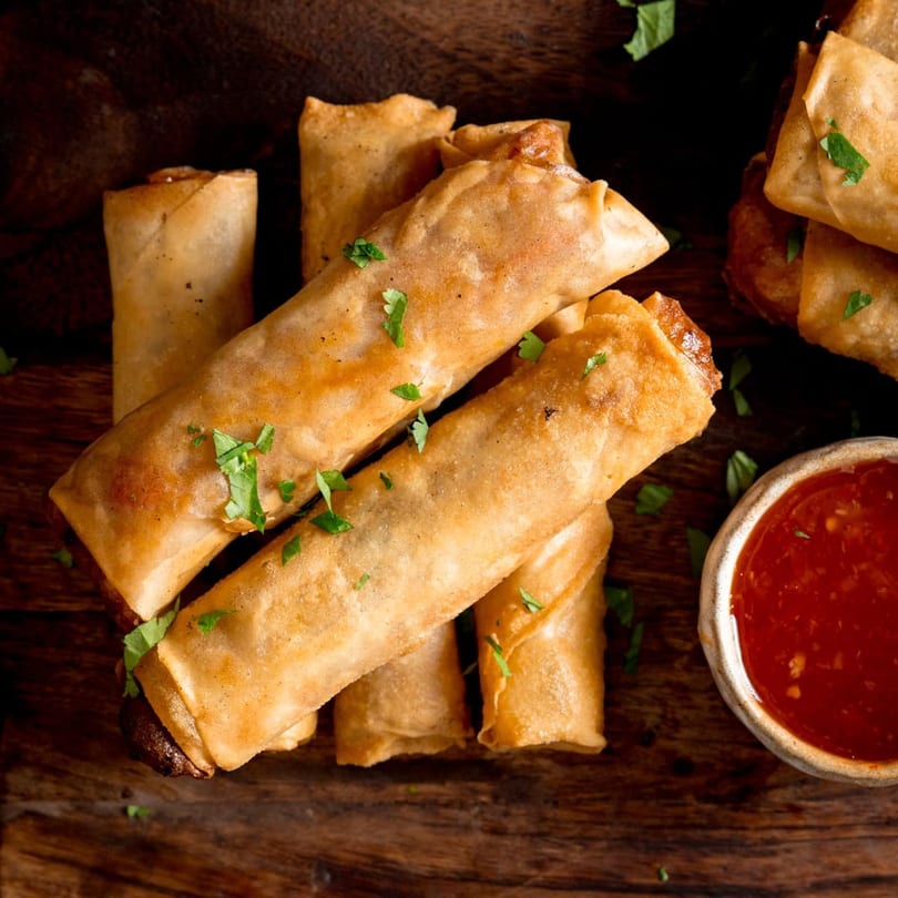 Crispy golden spring rolls garnished with parsley, served with a side of red dipping sauce.