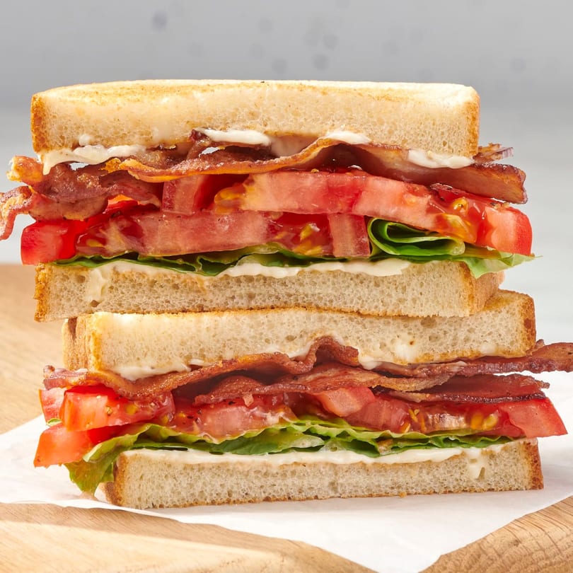 A tall, stacked BLT sandwich with crispy bacon, fresh lettuce, and sliced tomatoes on toasted bread.