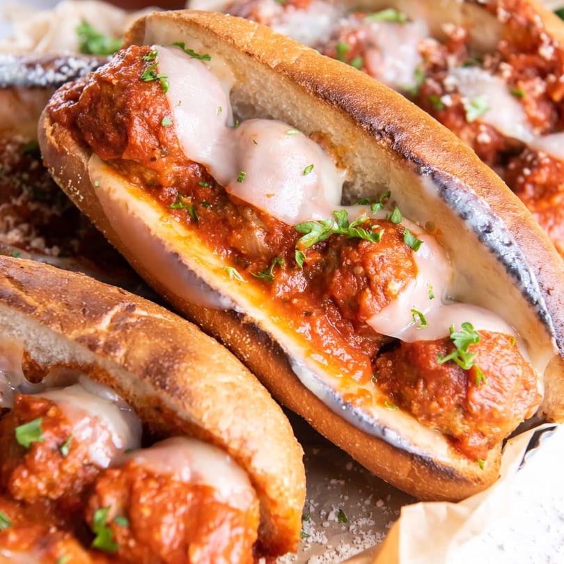 Close-up of a meatball sub with melted mozzarella cheese, marinara sauce, and parsley.