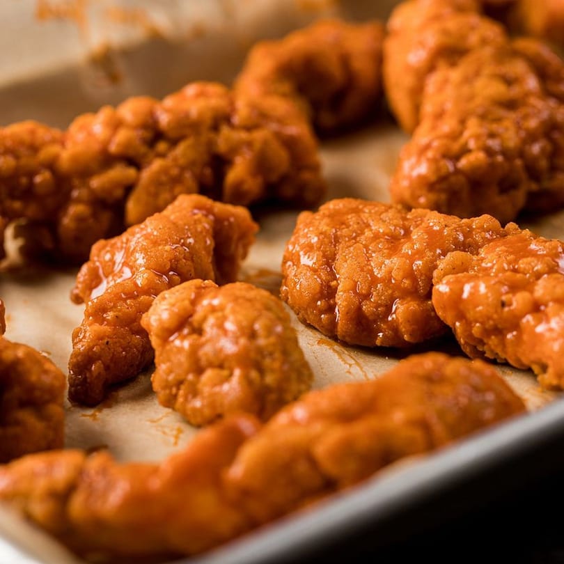 Close-up of several orange-glazed boneless chicken wings on a baking sheet from Sofiabella Pizzeria.